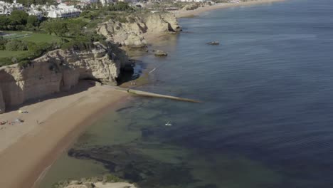 Fliegen-über-Zwei-Personen-Paddelboarden-An-Einem-Unglaublichen-Tropischen-Strand,-Umgeben-Von-Wunderschönen-Ozeanischen-Klippen,-Drohnenantenne