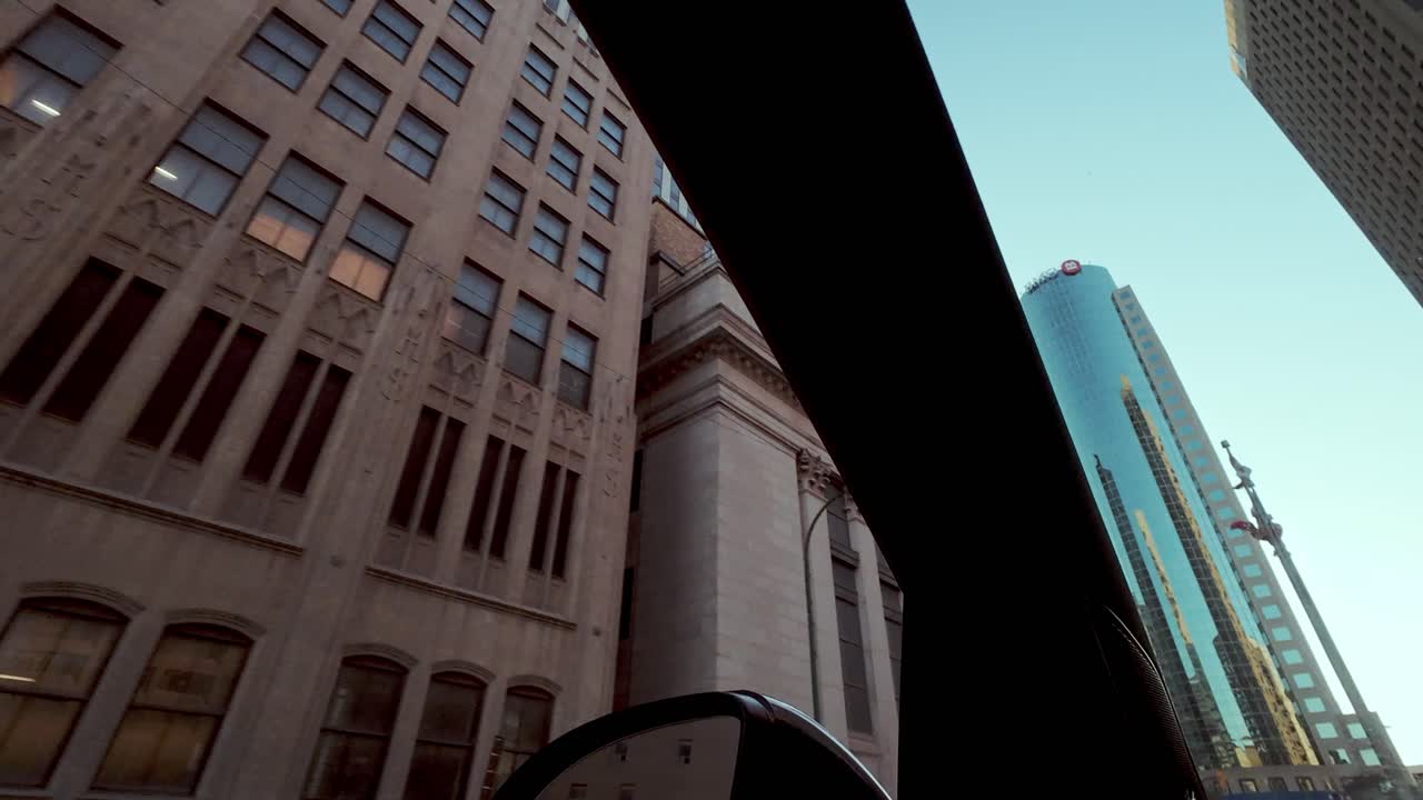 POV shot from car; vintage buildings pass to reveal modern glass and steel skyscrapers