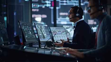 retrato de un especialista profesional en soporte técnico que trabaja en una computadora en una sala de control de monitoreo con pantallas digitales. el empleado usa auriculares con micrófono y habla en una llamada.
