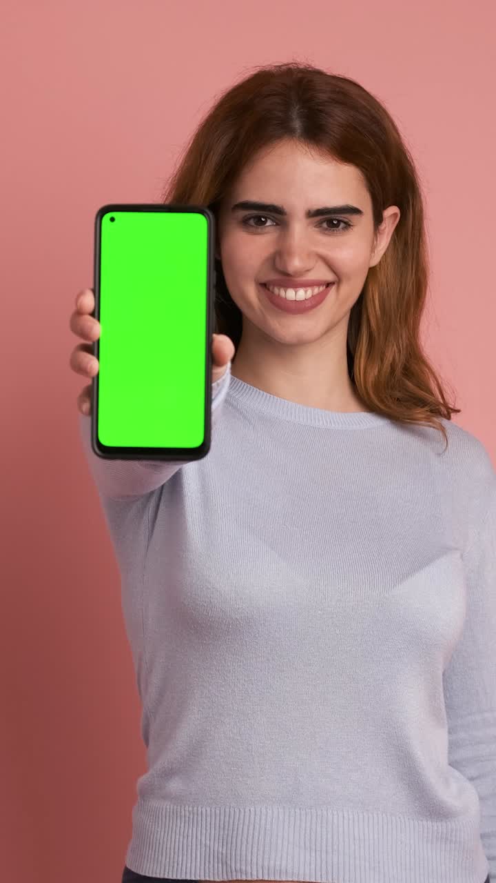 Woman showing cellphone with green screen in studio. Vertical Footage
