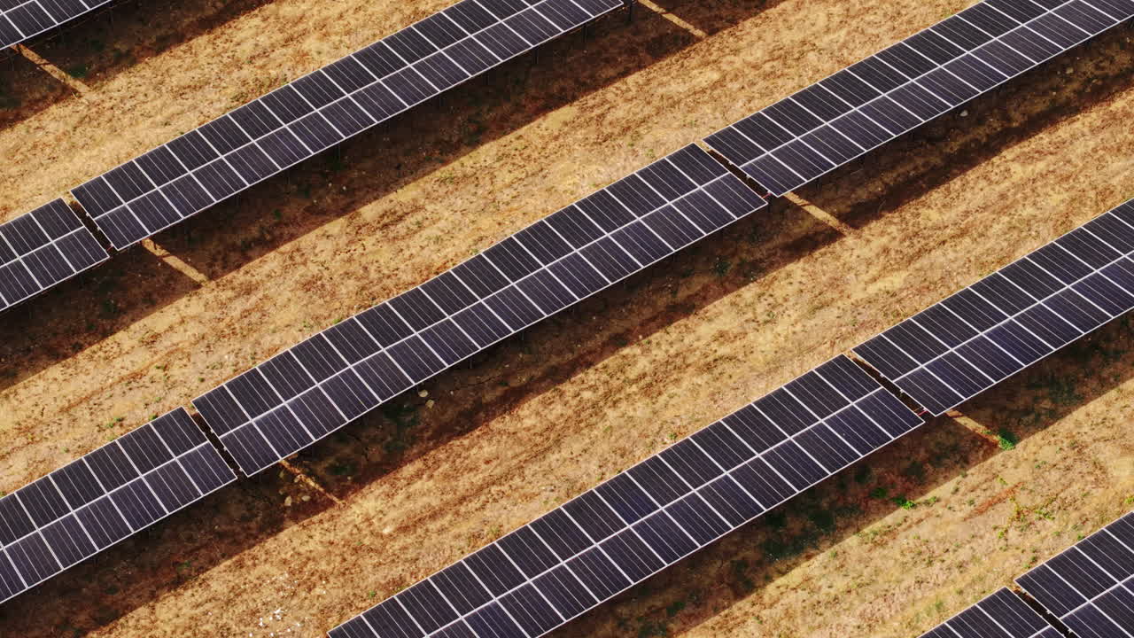 Lavt dronebillede, der starter med panorering og derefter drejer over et felt af solcellepaneler installeret på tør jord på Sicilien
