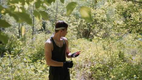 tourist wearing headband and fingerless gloves stands amid dense green forest under hot midday sun, pulling on gloves at waist with dappled light filtering through trees in summer scene