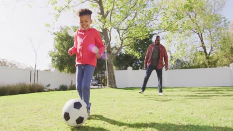 happy african american father and his son playing football in garden
