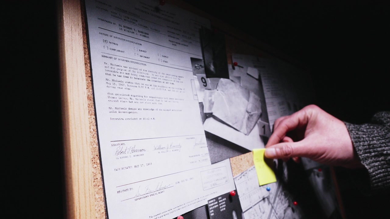 Hand applies a yellow evidence marker to an active investigation board, reinforcing themes of detective work, criminal analysis, and uncovering hidden connections.