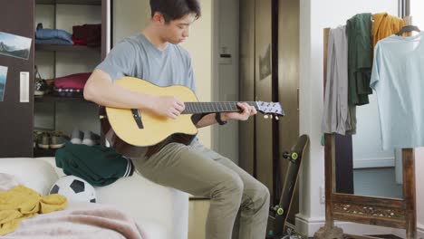 asian boy playing guitar sitting on the couch at home