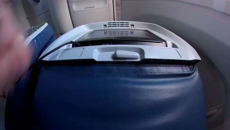 a hand plugs in black headphones into an entertainment screen on an airport chair