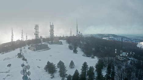 Schneebedeckter-Hügel-Mit-Zahlreichen-Kommunikationstürmen,-Umgeben-Von-Winterlichen-Bäumen