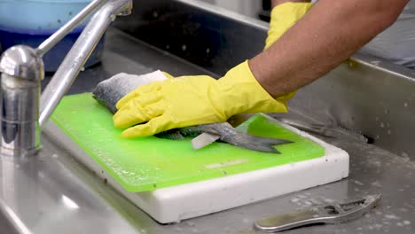 a skilled chef meticulously cleans and fillets a fresh fish on a bright green cutting board in a busy kitchen. the process showcases culinary artistry and fresh ingredients