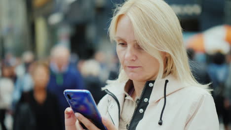 A-Sad-Middle-Aged-Woman-Uses-A-Smartphone-In-A-Crowd-Of-People-Loneliness-And-Depression-Concept