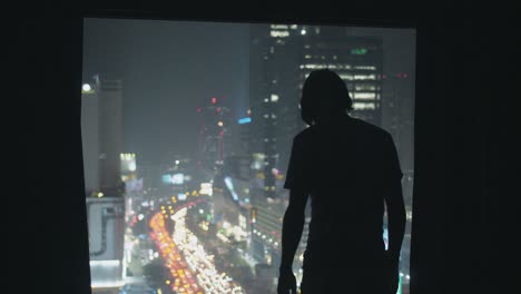 man opening curtains of city window at night