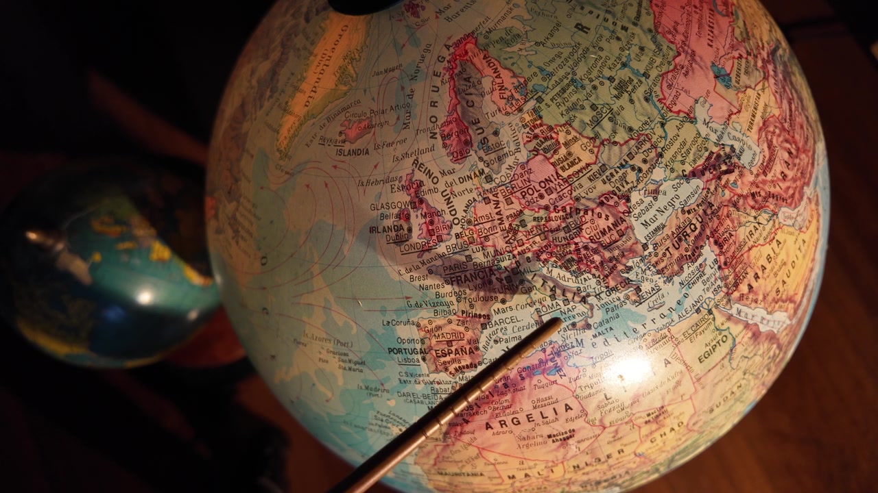 Un puntatore che indica l'Italia su un mappamondo vintage, evidenziando l'Europa meridionale e la regione mediterranea.