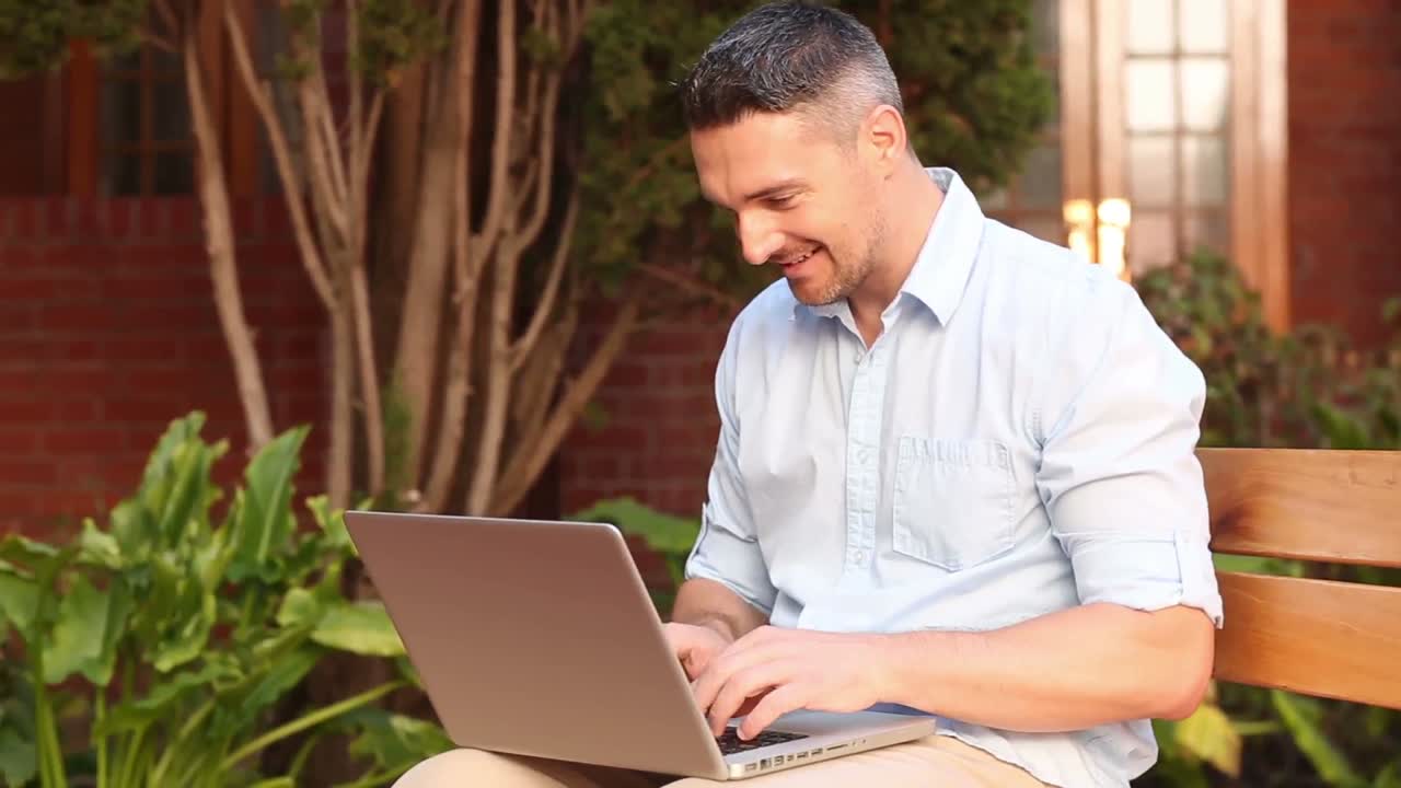 profesor feliz sentado en un banco usando una computadora portátil