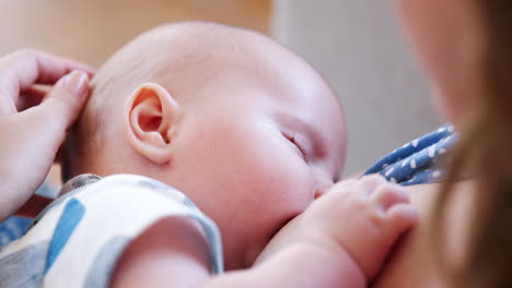 over the shoulder close up slow motion shot of mother sitting on sofa at home and breastfeeding baby