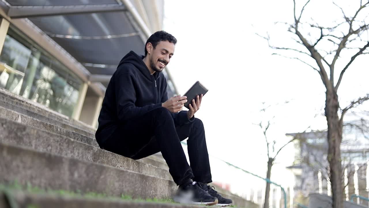 un joven sonriente con una tableta en la calle