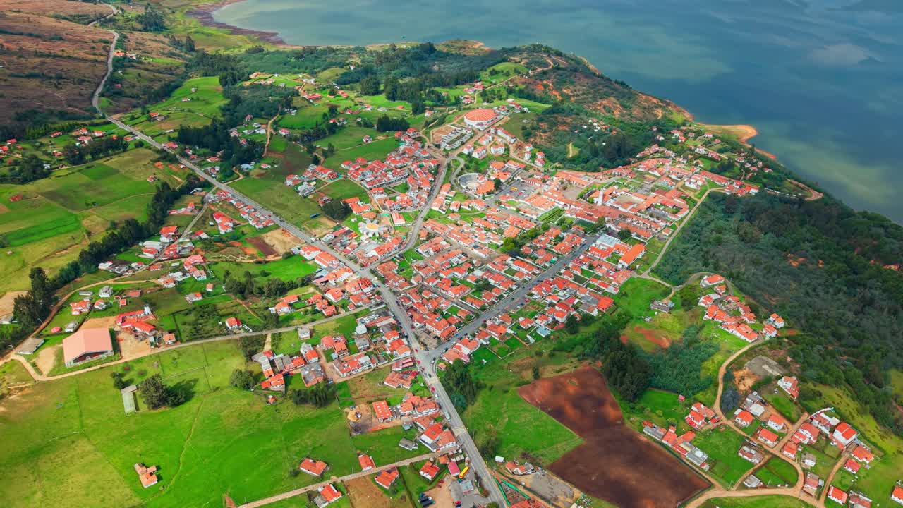 Guatavita’s charming village with red roofs nestled beside calm waters, viewed from above.