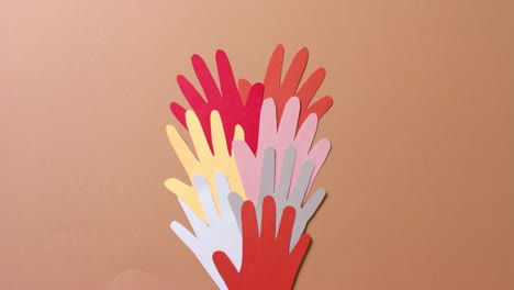 Close-up-of-hands-together-made-of-colourful-paper-on-brown-background-with-copy-space