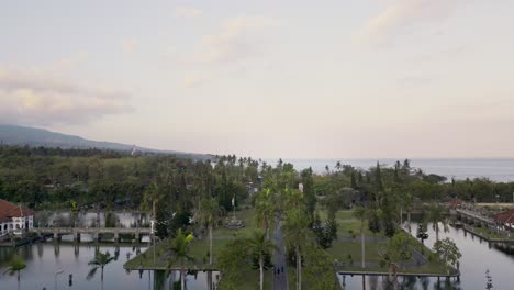 Aerial-view,-drone-shot,-of-a-tranquil-park-with-a-serene-lake,-surrounded-by-lush-greenery-and-a-backdrop-of-the-ocean-and-a-mountain-range