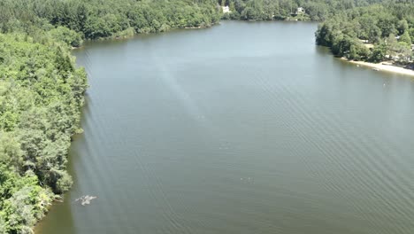 Aerial view high above tranquil lake winding through dense green forest landscape, Marcillac La Croisille, France