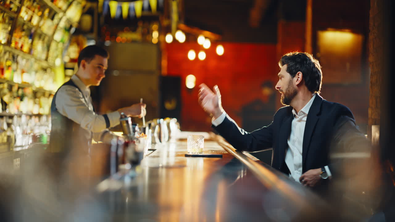 Primo piano di un uomo ubriaco che sorseggia un alcolico seduto al bancone di un bar. Un uomo rilassato che paga il cameriere
