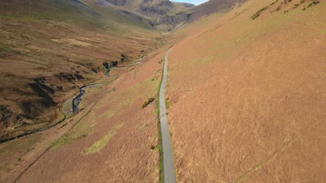 Flying-high-over-hikers-on-hillside-gravel-path-in-springtime-near-Force-Crag-Mine-Coledale-Beck-in-the-English-Lake-District