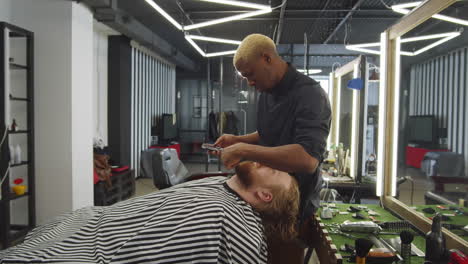barbero negro recortando la barba del hombre con cortadoras de cabello