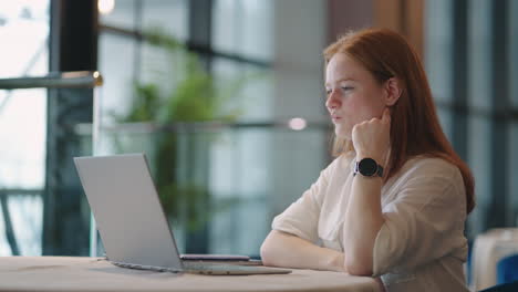 Eine-Fröhliche-Und-Positive-Junge-Frau-Mit-Roten-Haaren-Chattet-Online-Per-Laptop-Und-Sitzt-Zu-Hause-Oder-Im-Co-Working-Bereich