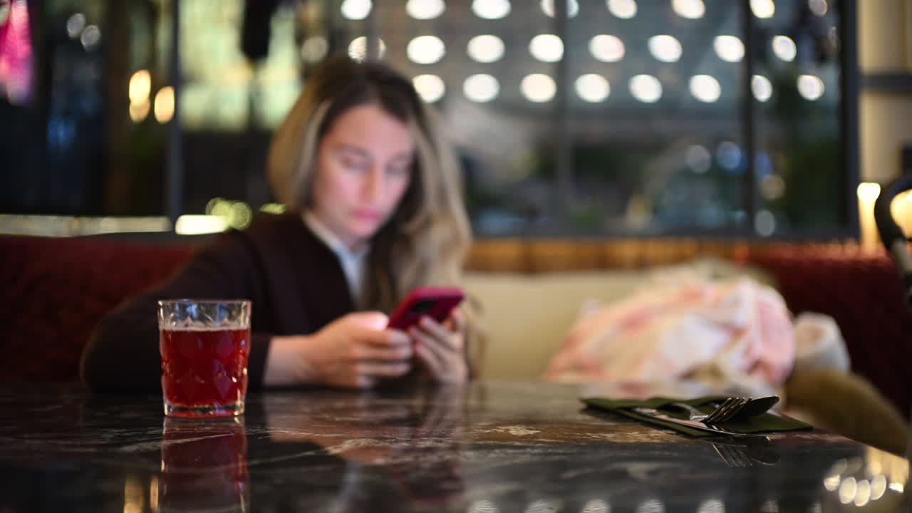 Woman seated indoors at a cafe table, focused on her smartphone