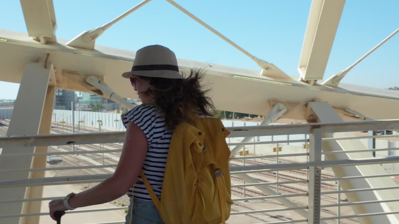 A woman is walking with a green suitcase on a bridge. The bridge is long and has a lot of space