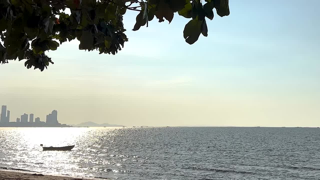 A serene ocean scene with a boat and city skyline under a clear sky, framed by tree leaves.
