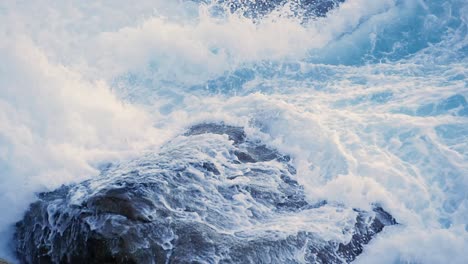 foamy waves crashes through rocks on coastline during summer. - close up
