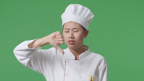 close up of asian woman chef showing thumbs down gesture to camera while standing in the green screen background studio