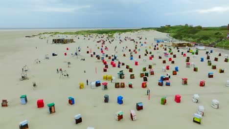 Close up flyover Borkum island beach, packed with colorful beach chairs called Strandkörbe, reveal lush green coastal vegetation