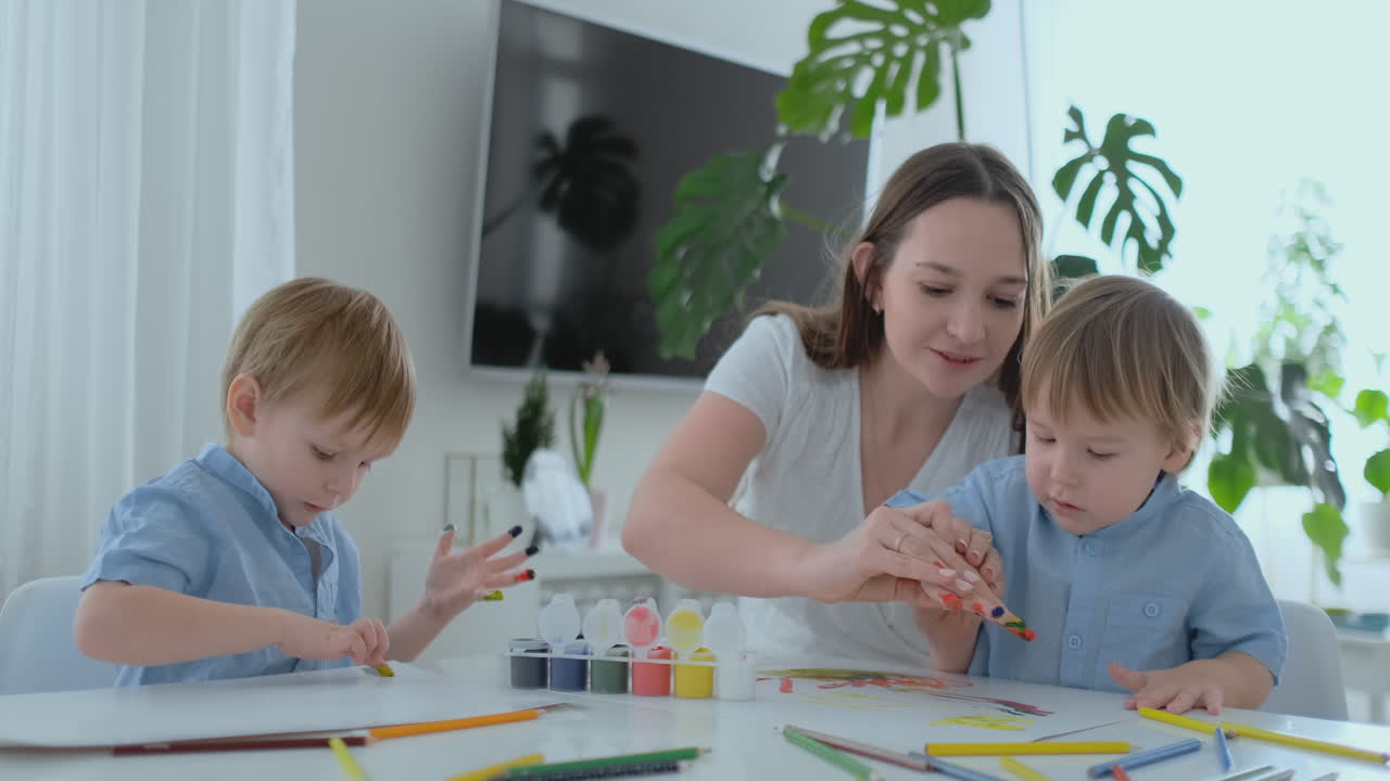 Mom helps her sons to develop creative skills and is engaged with them to create drawing paints with the help of fingers. Child development. Creative family. Loving mom
