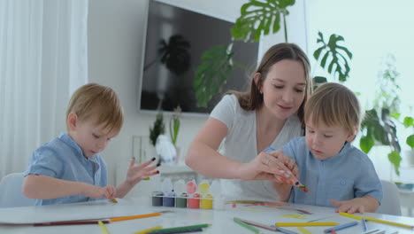 mom helps her sons to develop creative skills and is engaged with them to create drawing paints with the help of fingers. child development. creative family. loving mom