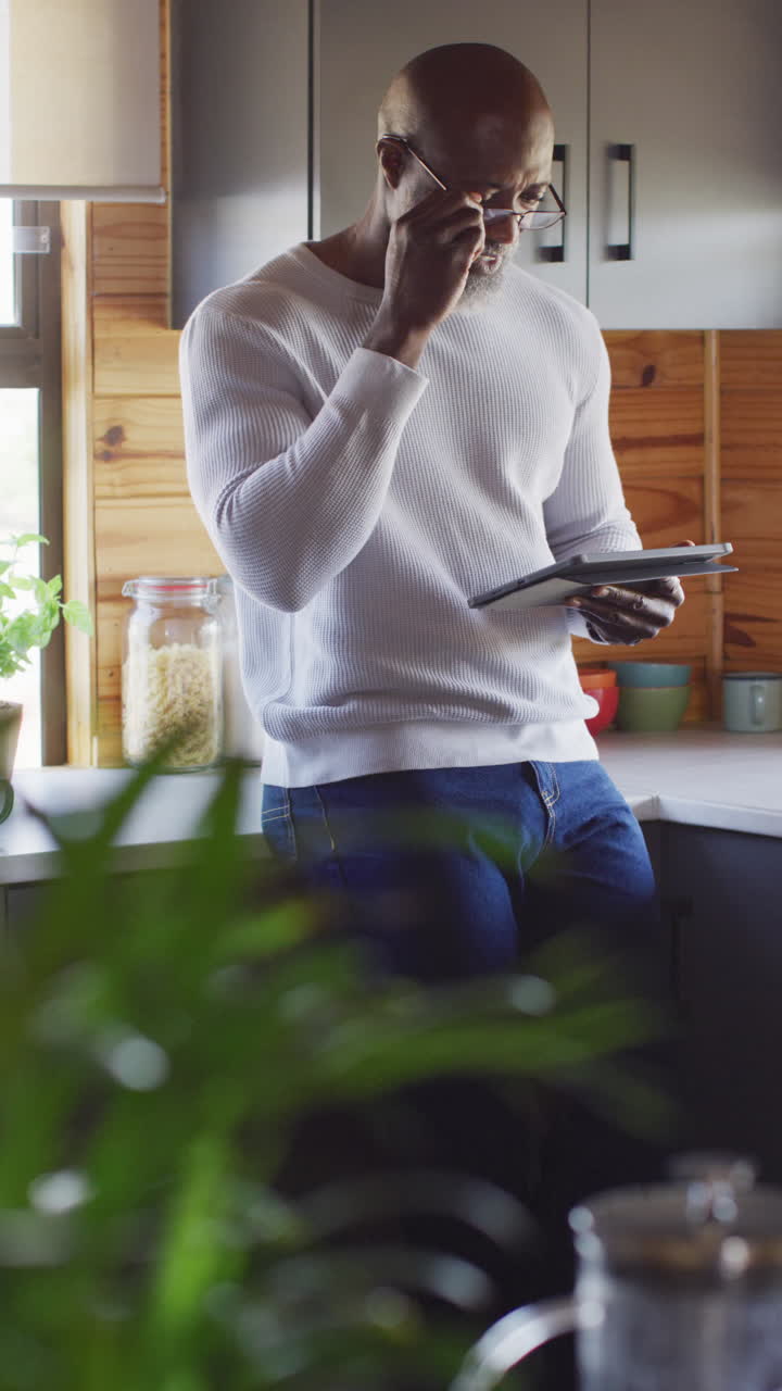 Vertical video of senior african american man spending time in log cabin using tablet