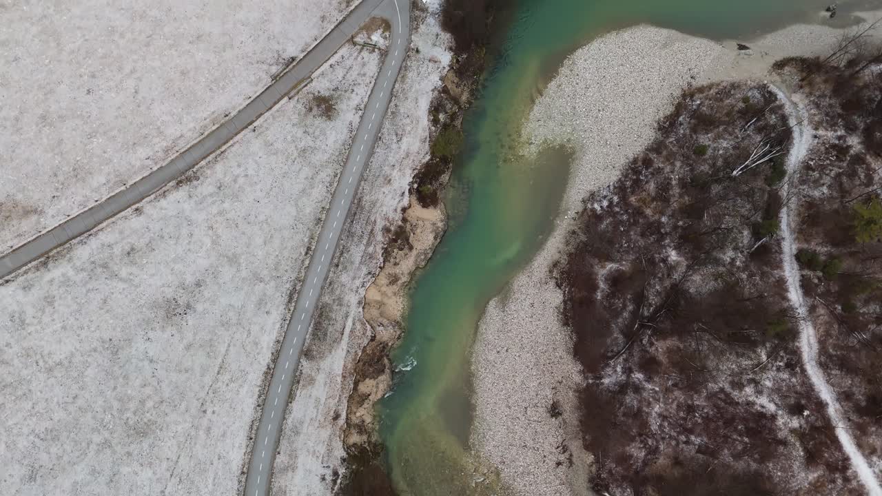 Sava Bohinjka-floden flyder gennem en sneklædt alpedal nær Kamnje i Triglav Nationalpark, Slovenien, med turkisblåt vand og skovklædte bredder set fra et top-down droneperspektiv fra luften