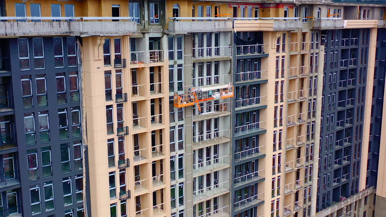 High-rise architecture under construction. Workers on the outdoor lift doing the beautiful facade of multi-storey building.