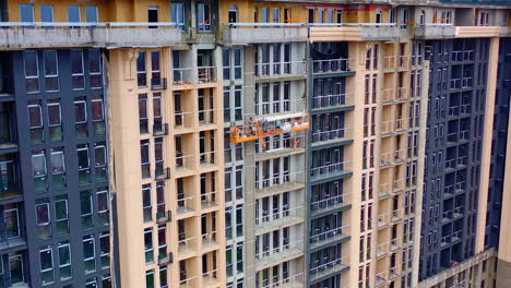 high-rise architecture under construction. workers on the outdoor lift doing the beautiful facade of multi-storey building.