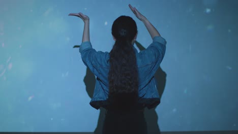 mujer visitando una exposición de arte inmersivo interactuando con imágenes de agua proyectadas en la pared