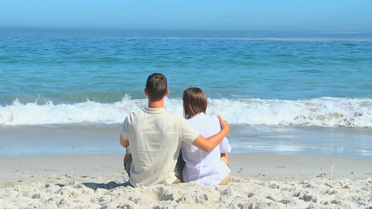 바다 앞에 앉아 안고 있는 귀여운 커플