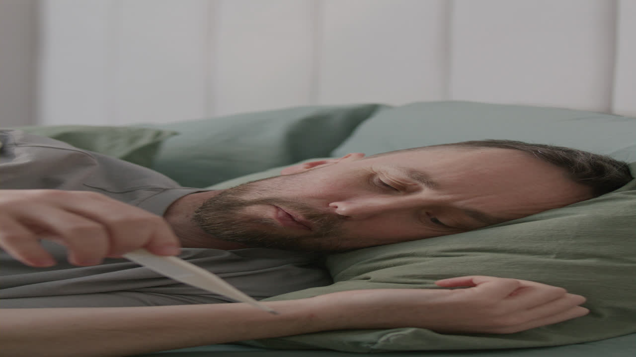 Sick Man Wakes Up in Bed, Coughs, and Checks His Temperature