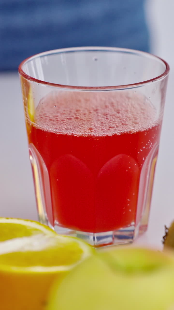 Glass of fresh red juice among fruits. Female's hand taking glass of freshly squeezed juice from the table. Dieting concept. Close-up. Vertical video