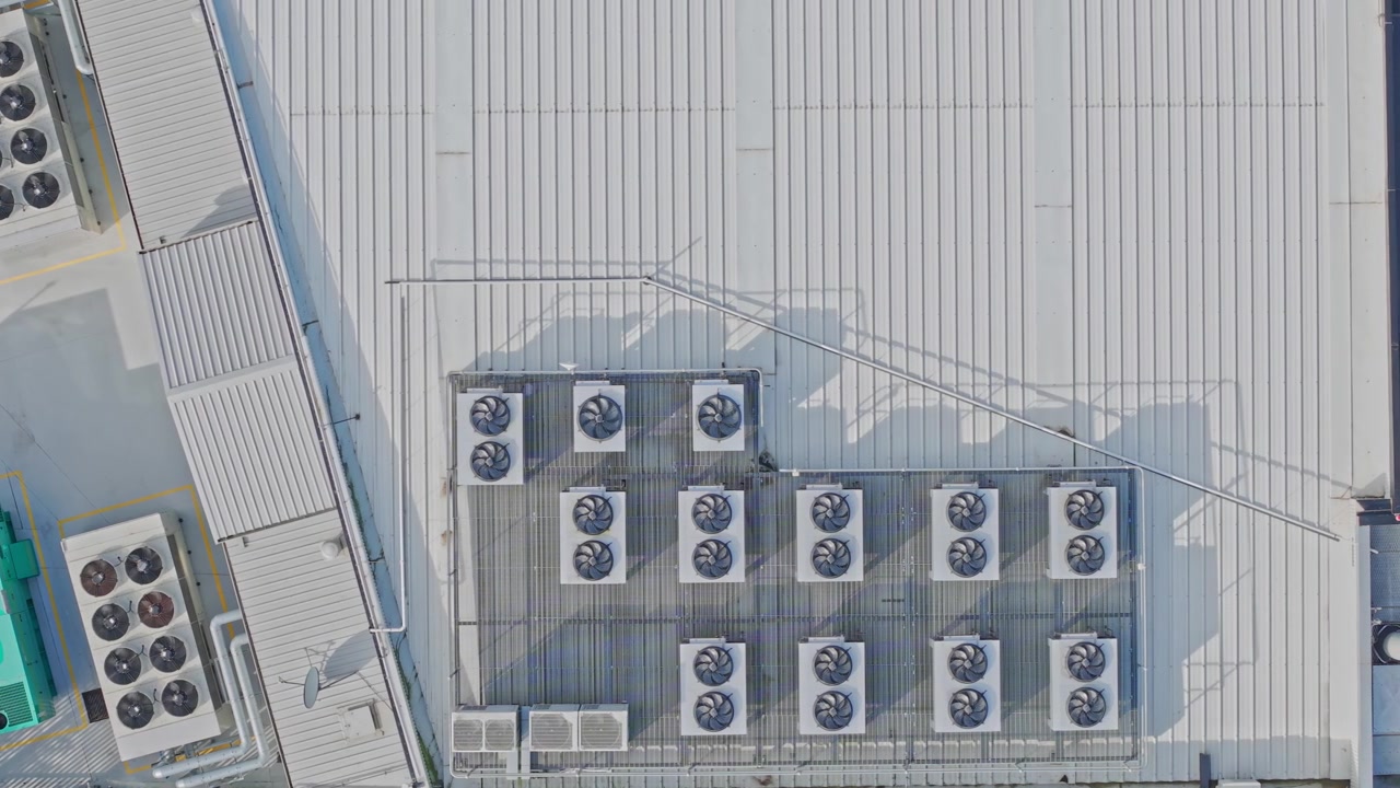 Video luminoso dall'alto con drone rivela il tetto di un moderno data center, pieno di unità di raffreddamento HVAC, ventilatori e tubazioni industriali sotto la luce chiara del giorno in un ambiente pulito e ordinato.
