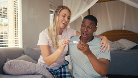 excited couple in bedroom at home celebrating positive pregnancy test result