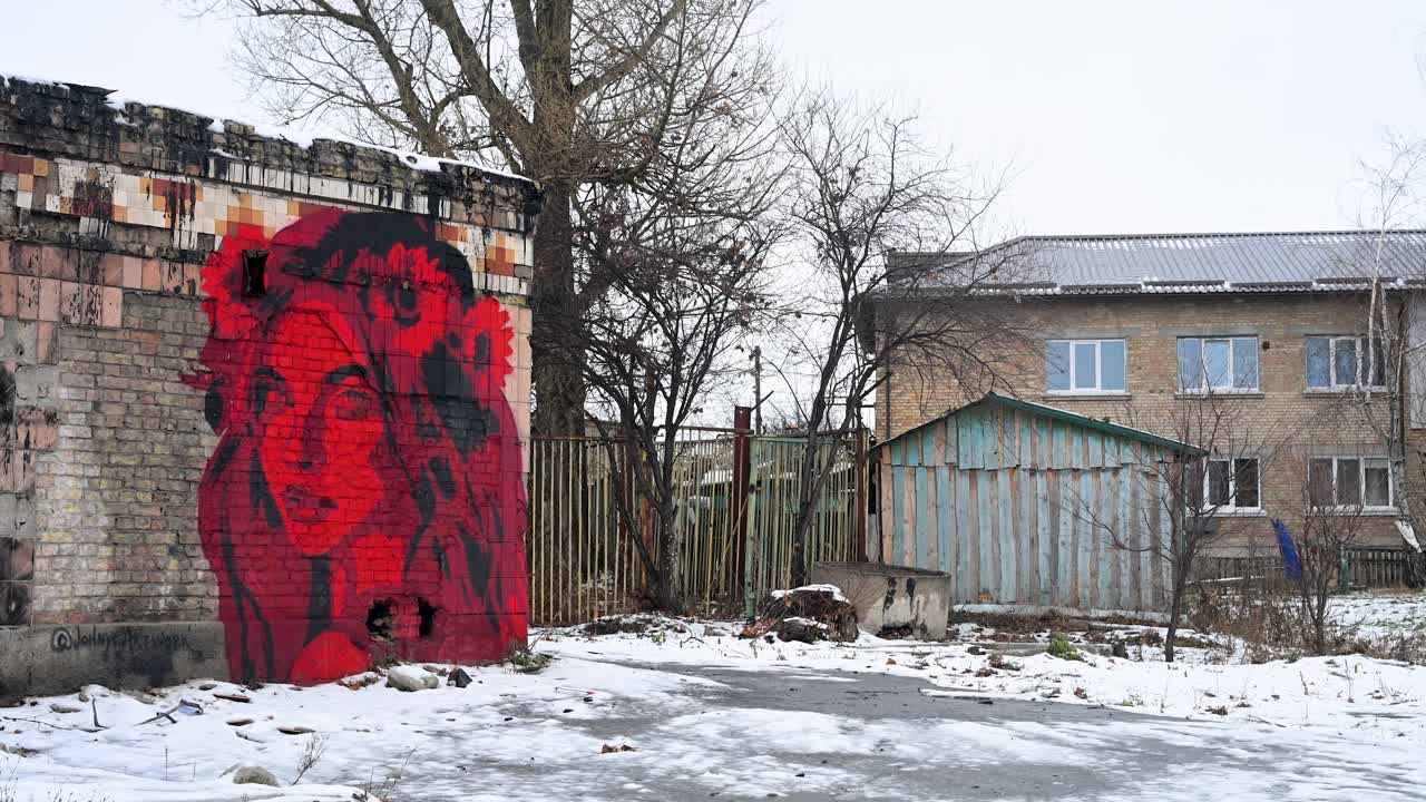 A winter scene in Irpin, Ukraine, shows red graffiti of a woman in Ukrainian folk clothing, painted over the damage caused by intense battles between Ukrainian and Russian forces in the war-torn area.