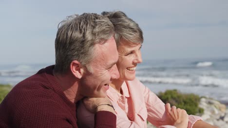 Caucasian-couple-enjoying-free-time-by-sea-on-a-sunny-day-sitting-and-embracing