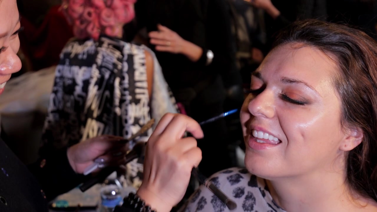 Professional stylist applying makeup to model with long brown curly hair - pink haired model behind - wedding, bridal, empowerment, focus - 4K, 23.98fps