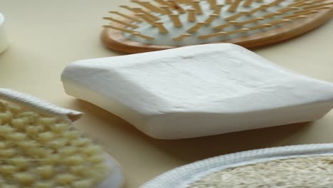 una vista de cerca de una barra blanca de jabón junto a un pincel de madera, loofah y otros accesorios de baño