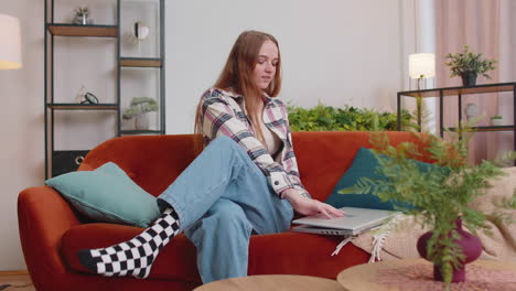 caucasian young woman sitting on sofa opening laptop pc starting work online in living room at home