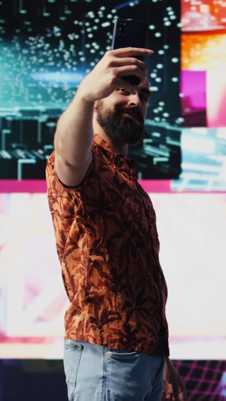 Vertical Video Young carefree man takes selfies and videos surrounded by fun neon lights